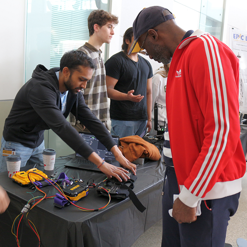 three men behind an exhibit table with one man on-looking