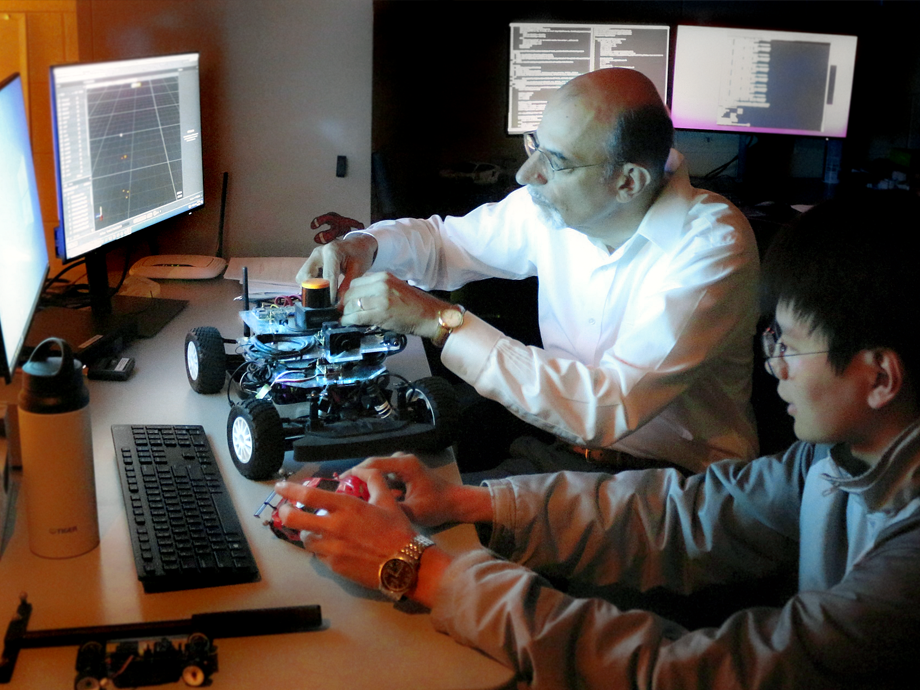 two men in front of a computer working on a robotic car